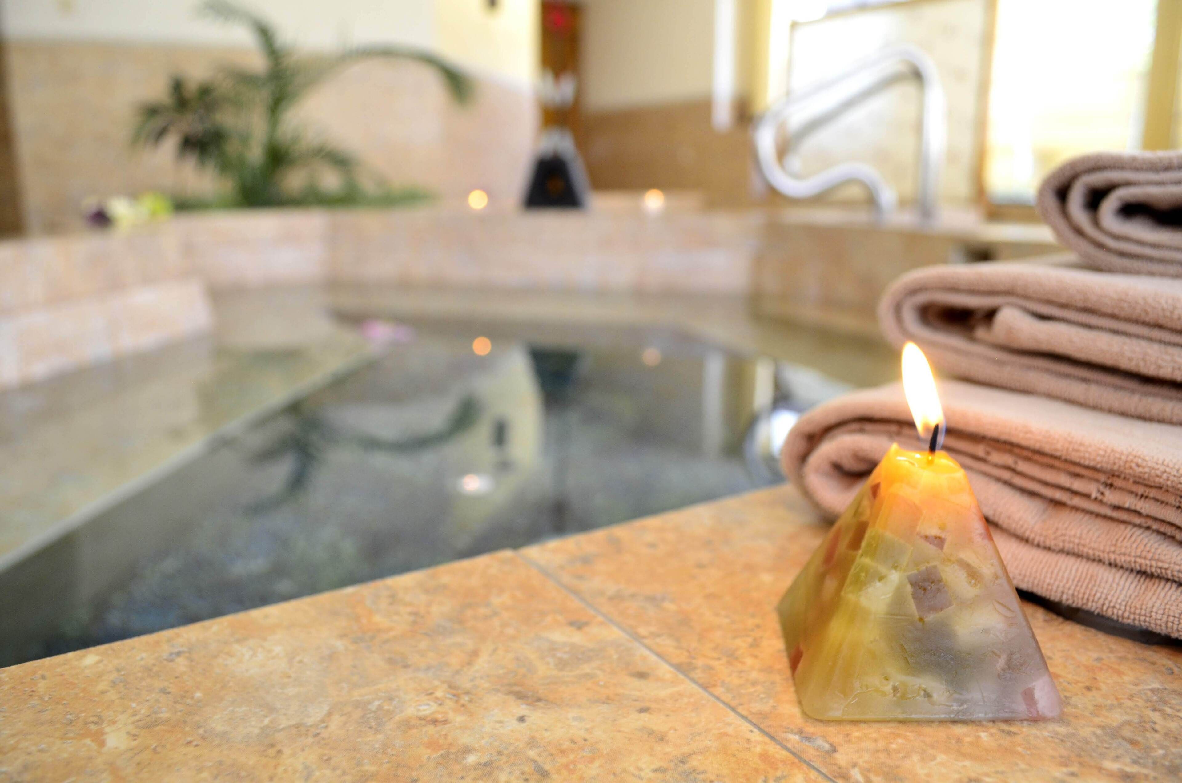 A candle on a tiled surface near a pool, with towels stacked beside it.