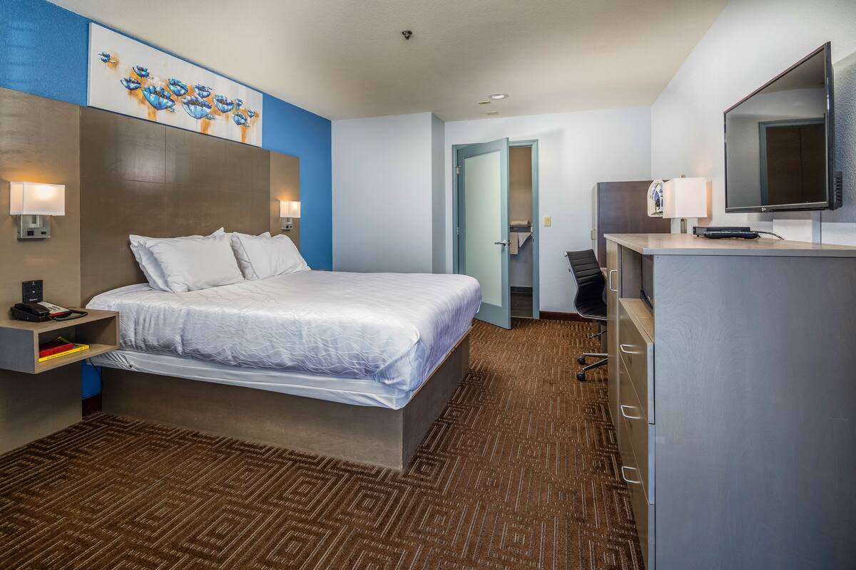 A hotel room with a bed, bedside lamps, a flat-screen TV, a desk with a lamp, and a wardrobe.