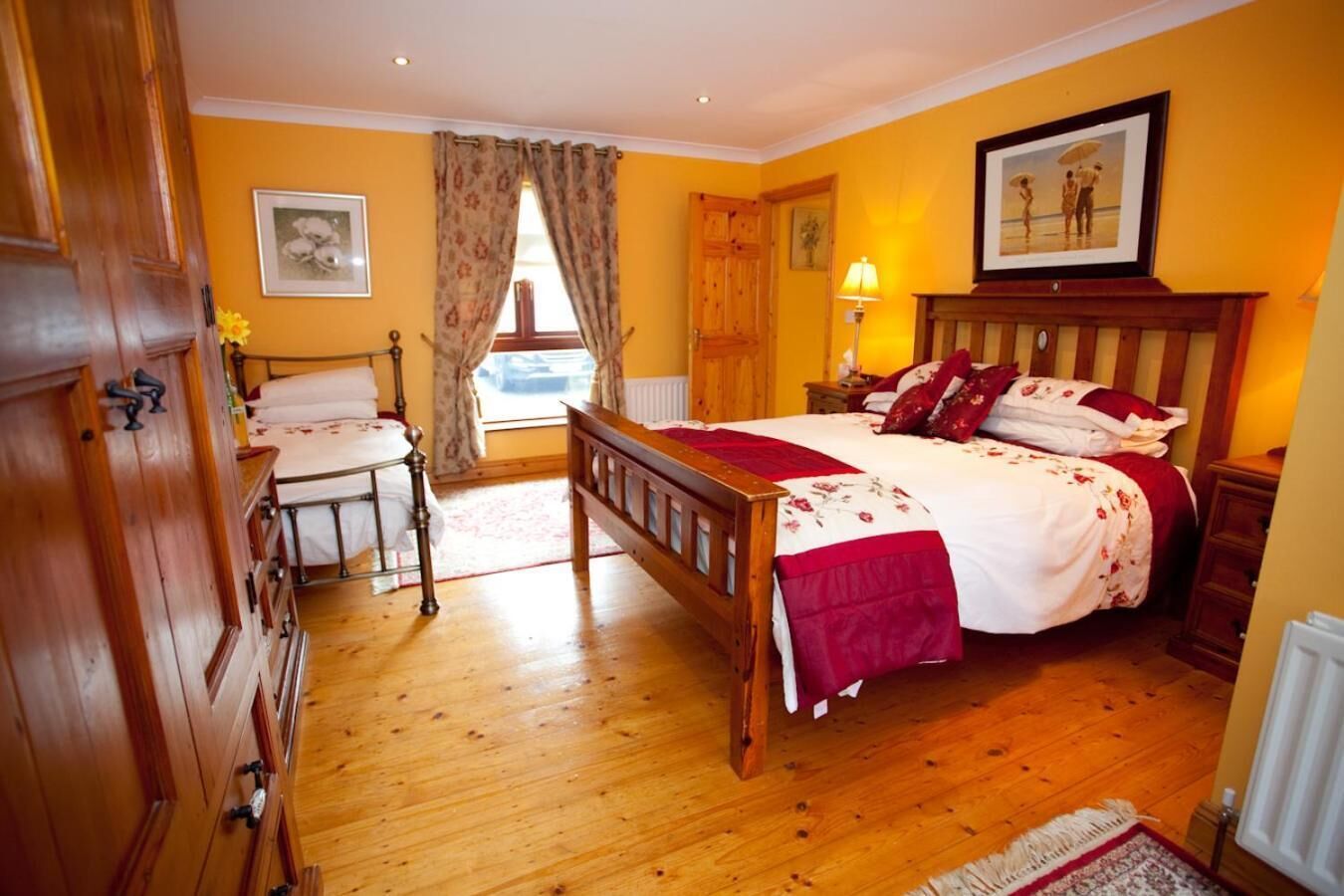 A bedroom with a wooden bed, a wooden dresser, a nightstand, and a window with curtains.