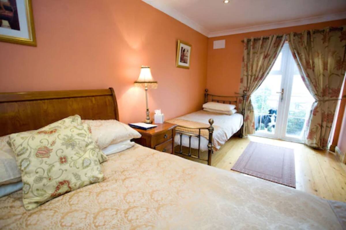 A bedroom with two beds, a nightstand, a lamp, and a window with curtains.