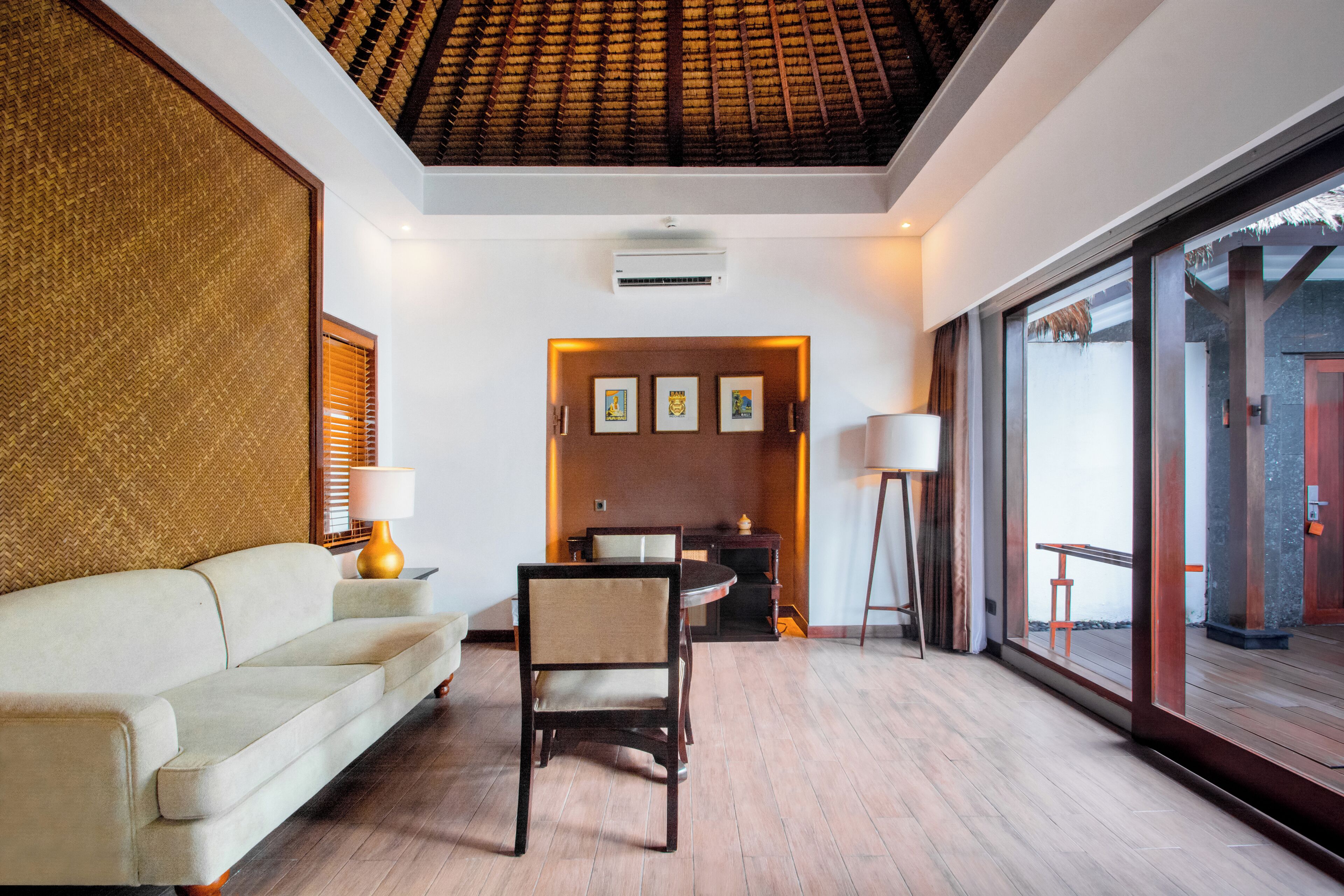 A modern hotel room with a sofa, a dining table, and chairs. There is a large window with a view of the outside.