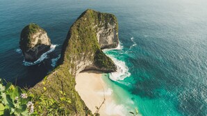 Paisagem costeira com uma formação rochosa imponente e uma praia.