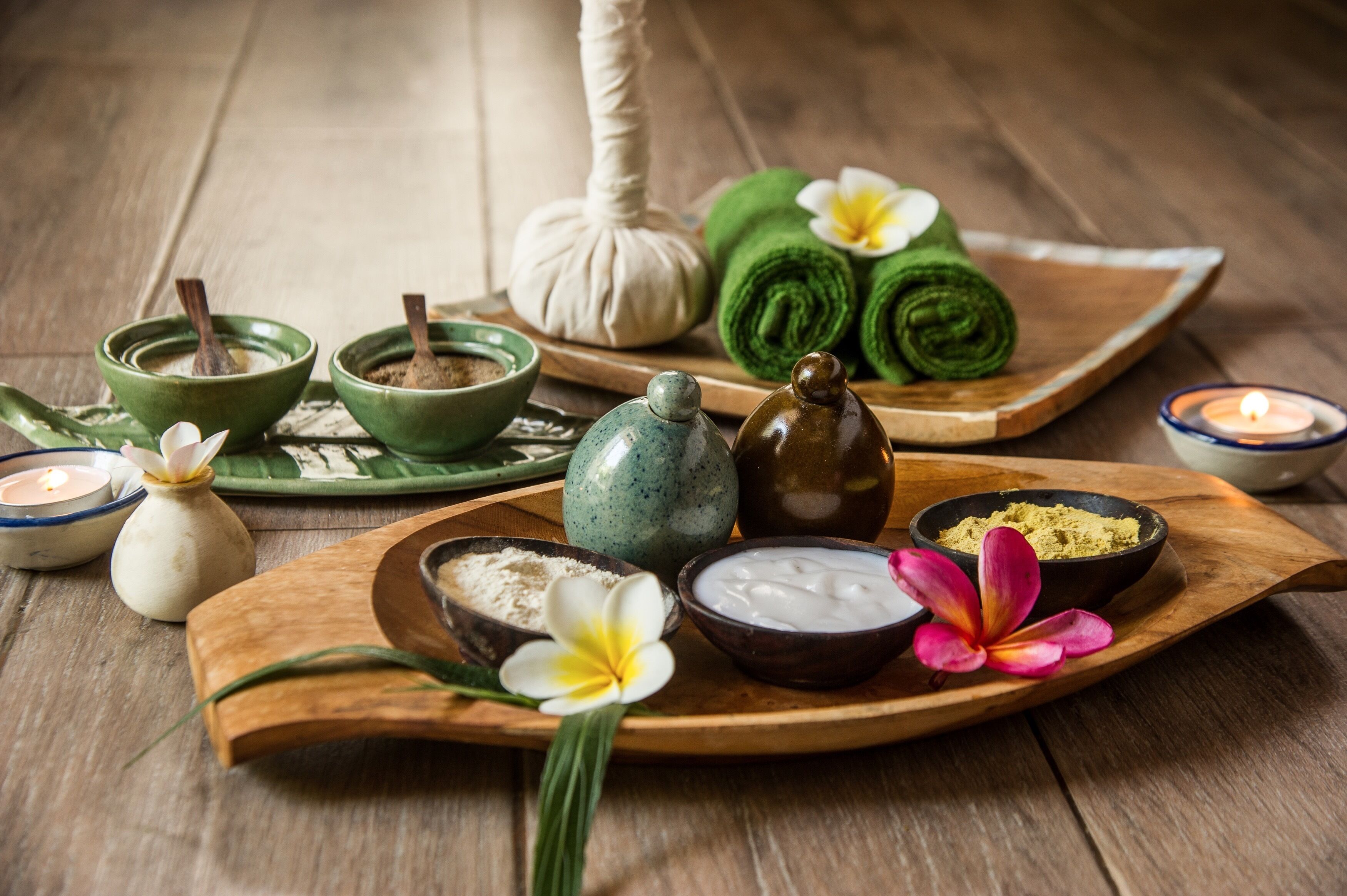 Una bandeja de madera con diversos productos de spa, entre ellos recipientes con aceite, una toalla verde enrollada y una vela pequeña.