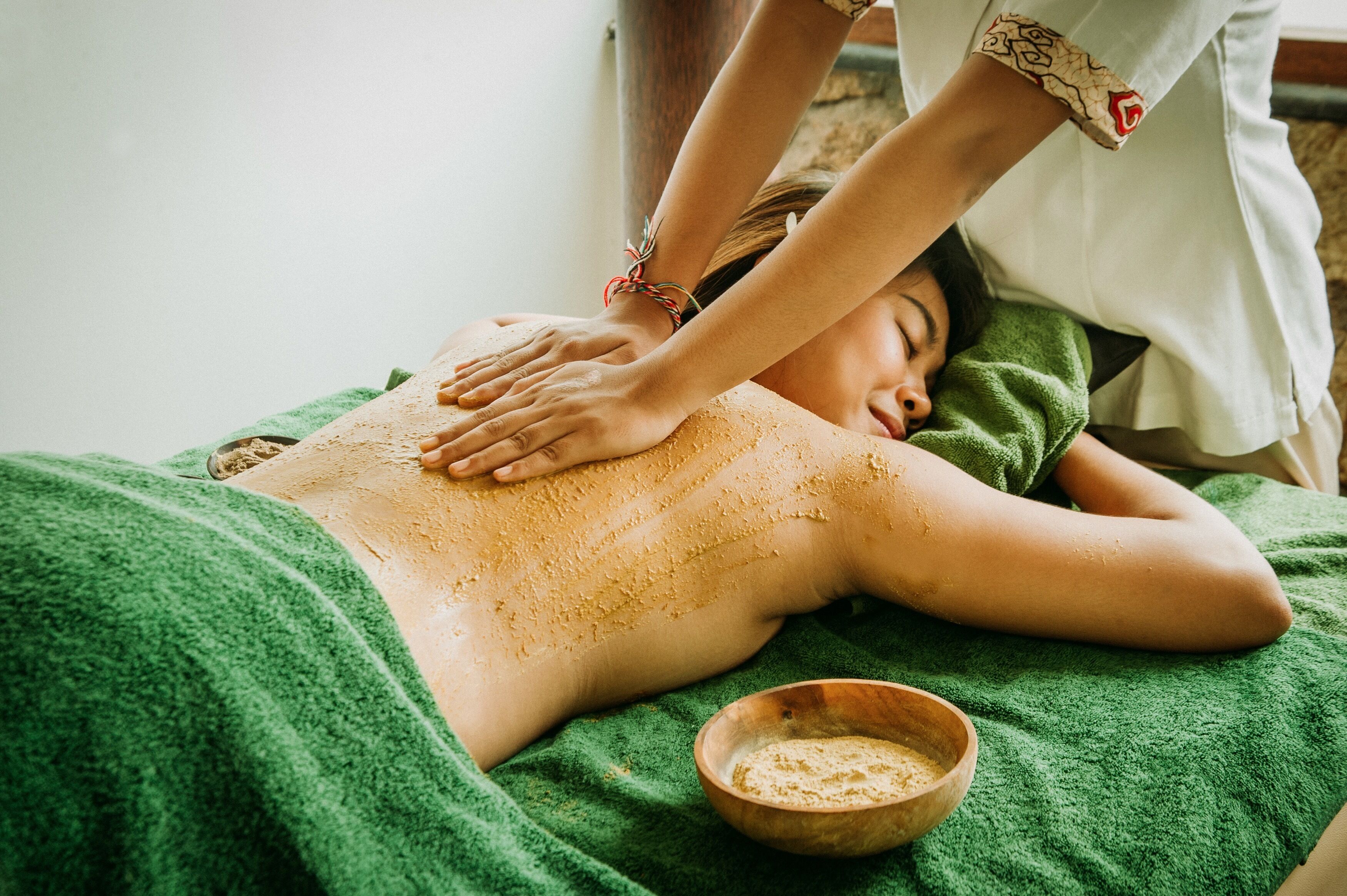 A person receiving a back massage on a green towel, with a wooden bowl nearby.