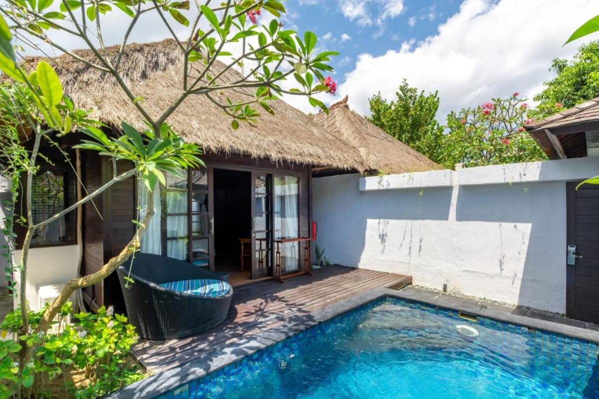 Un espace aménagé au bord de la piscine, avec une structure à toit de chaume, une chaise en osier et une terrasse en bois.