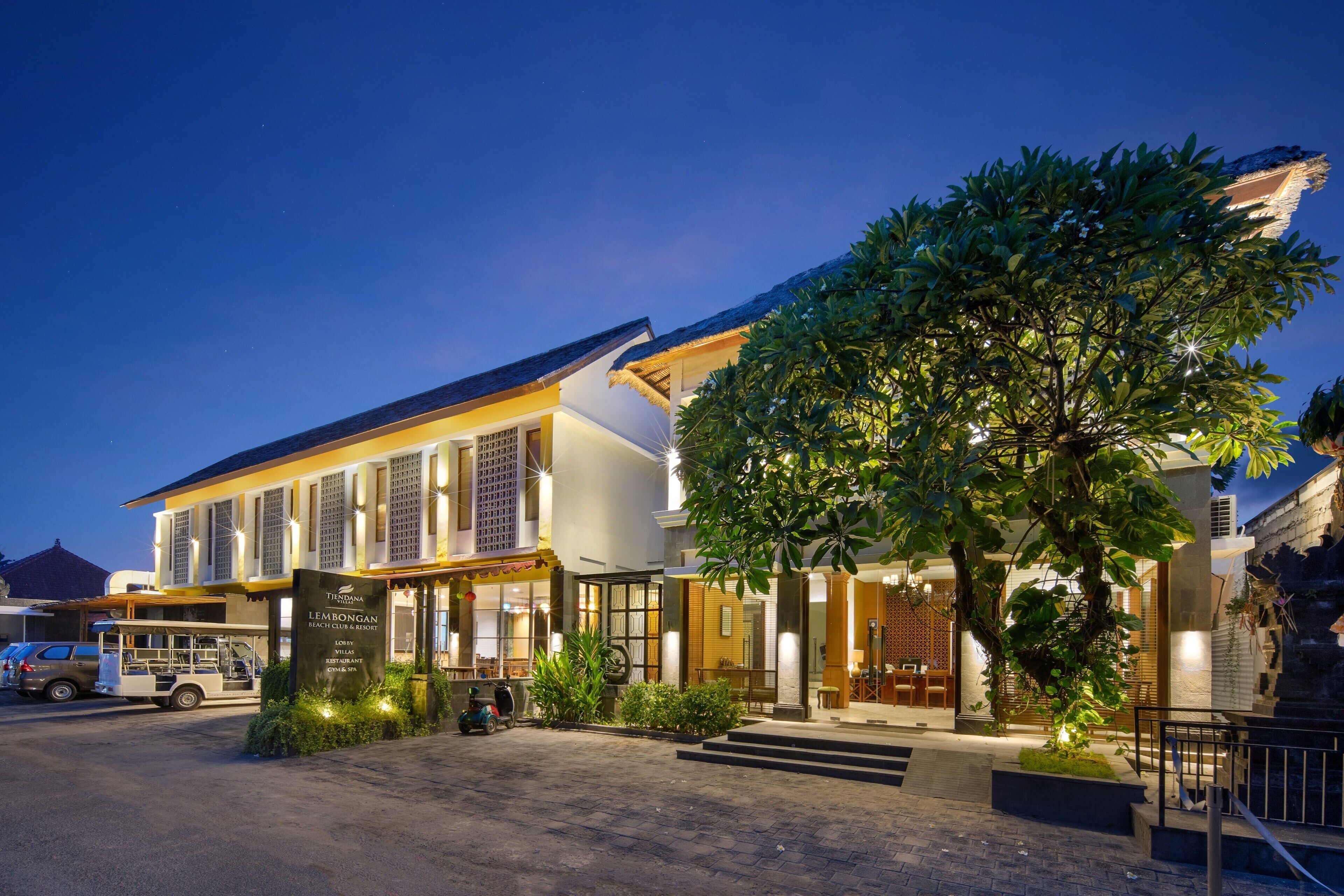 A hotel with a large tree in front, a covered outdoor seating area, and a sign indicating a restaurant.