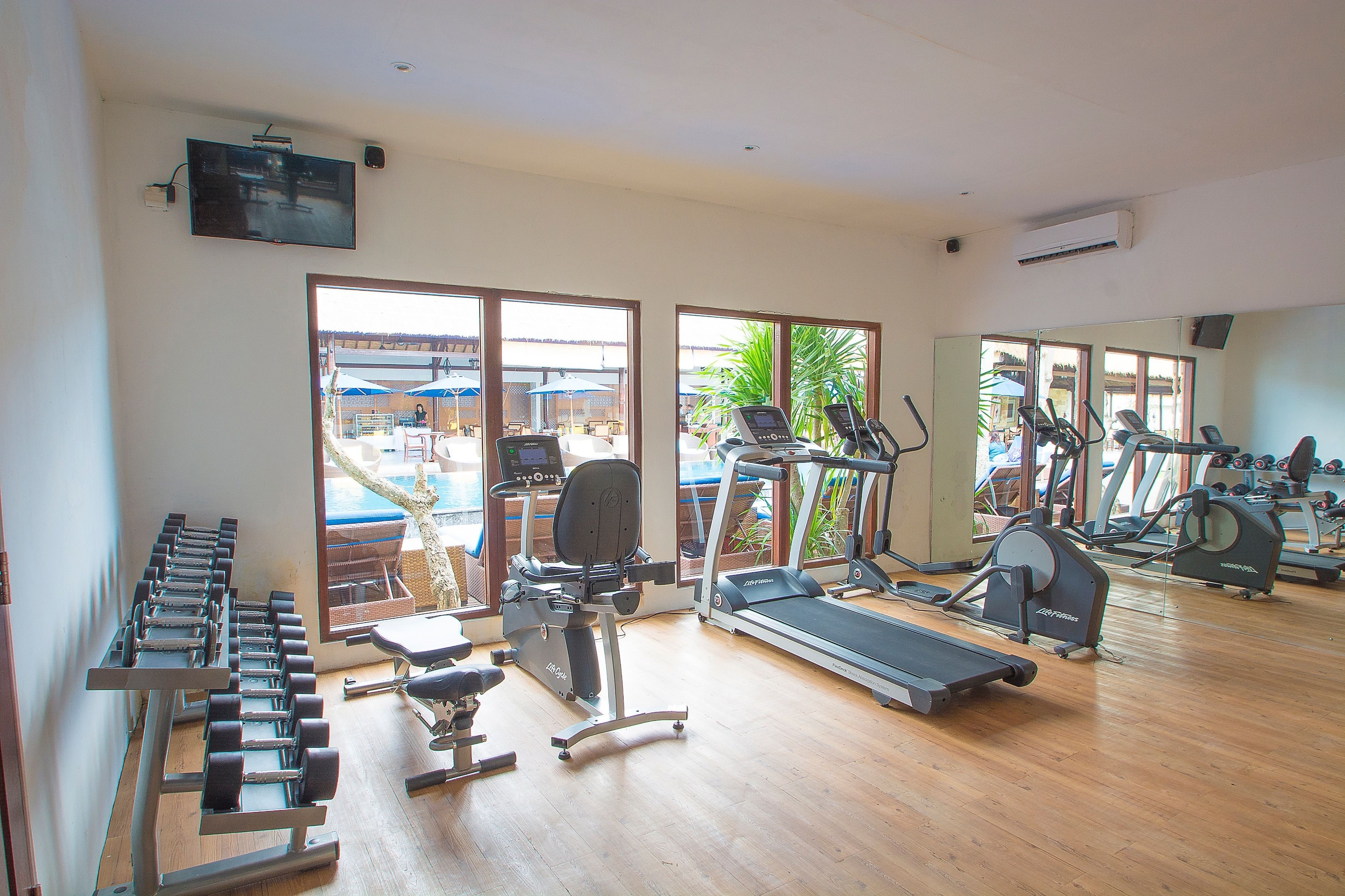 A gym with various exercise equipment, large windows, and a view of the outside.