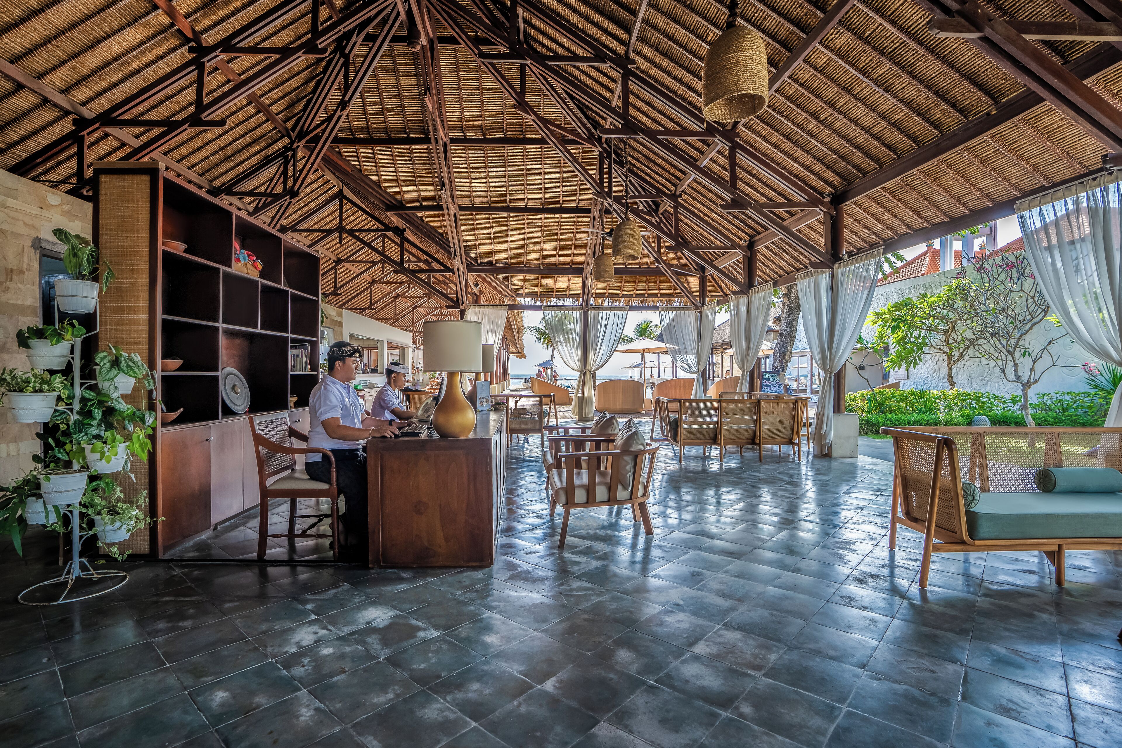 A spacious indoor area with a high ceiling and a wooden structure. There are several wooden chairs and tables, and a reception desk with a person behind it.