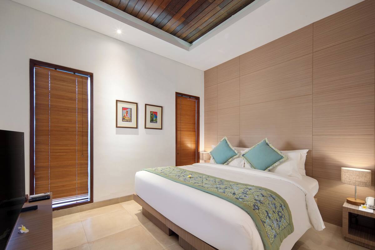 Une chambre d’hôtel moderne avec un grand lit, une tête de lit en bois et un téléviseur à écran plat posé sur une commode en bois.