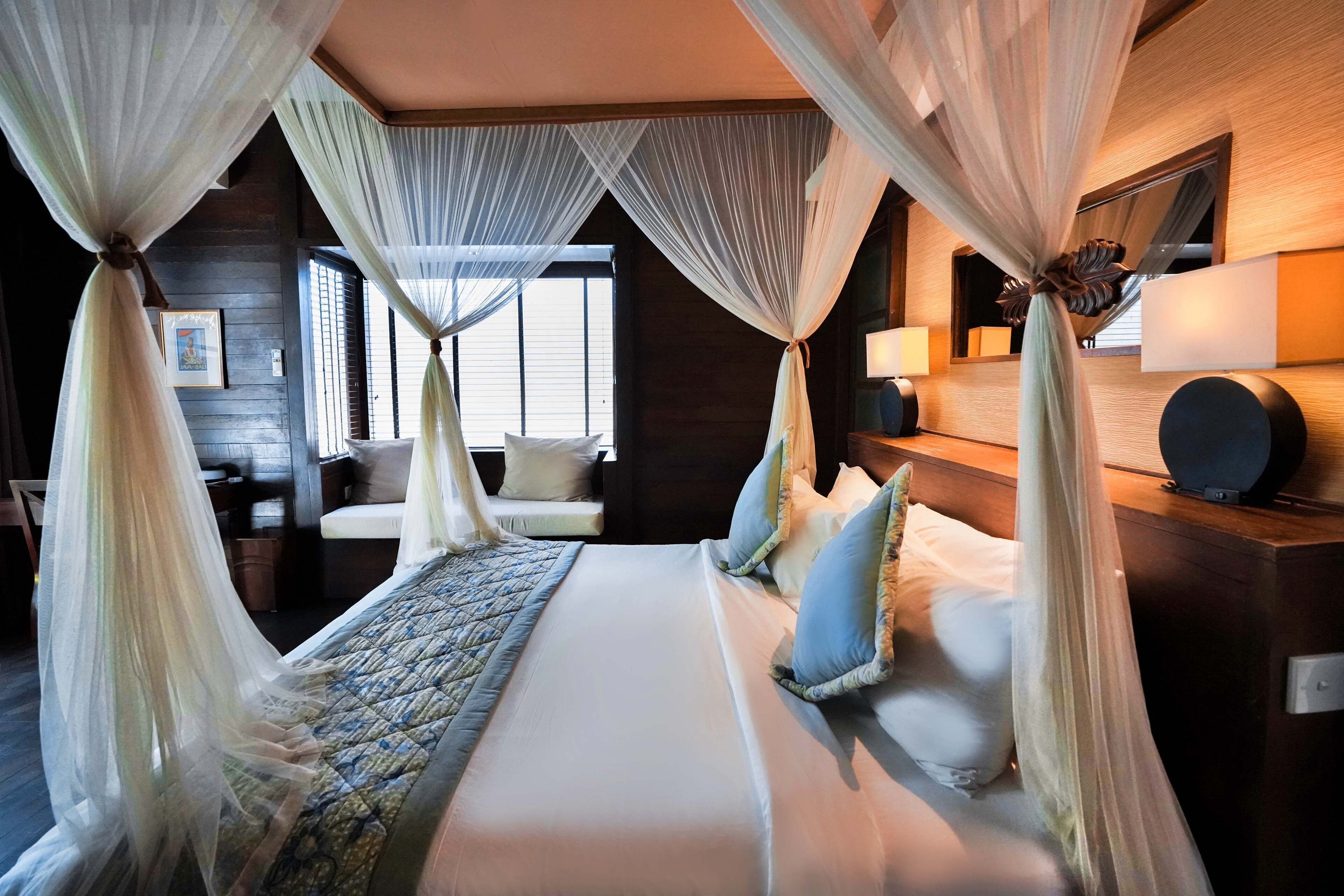 Un dormitorio con una cama grande, una mesita de noche, una lámpara y una ventana con persianas.