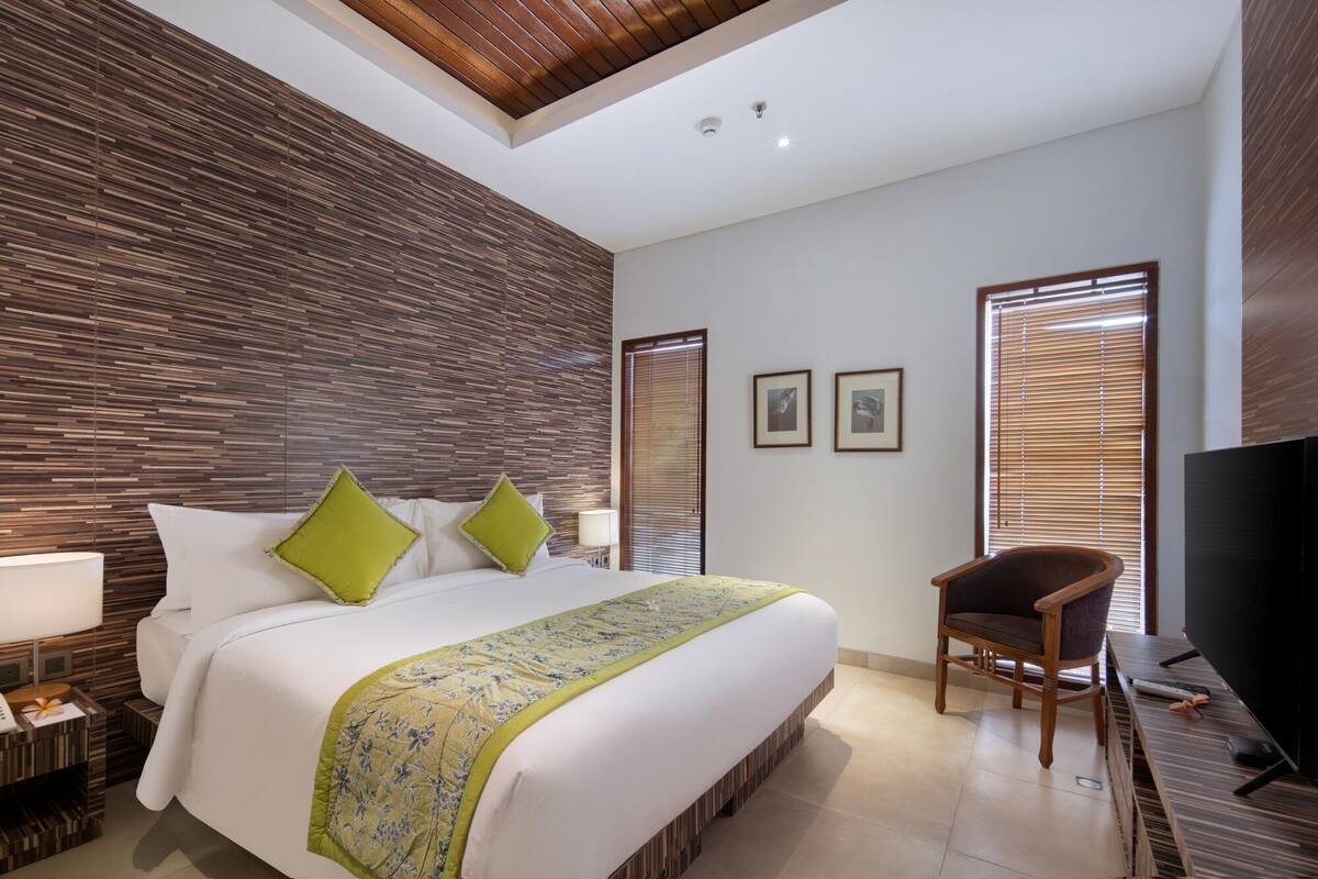 Une chambre d’hôtel moderne avec un grand lit, un mur lambrissé en bois, deux fenêtres équipées de stores, une chaise en bois et un téléviseur à écran plat.
