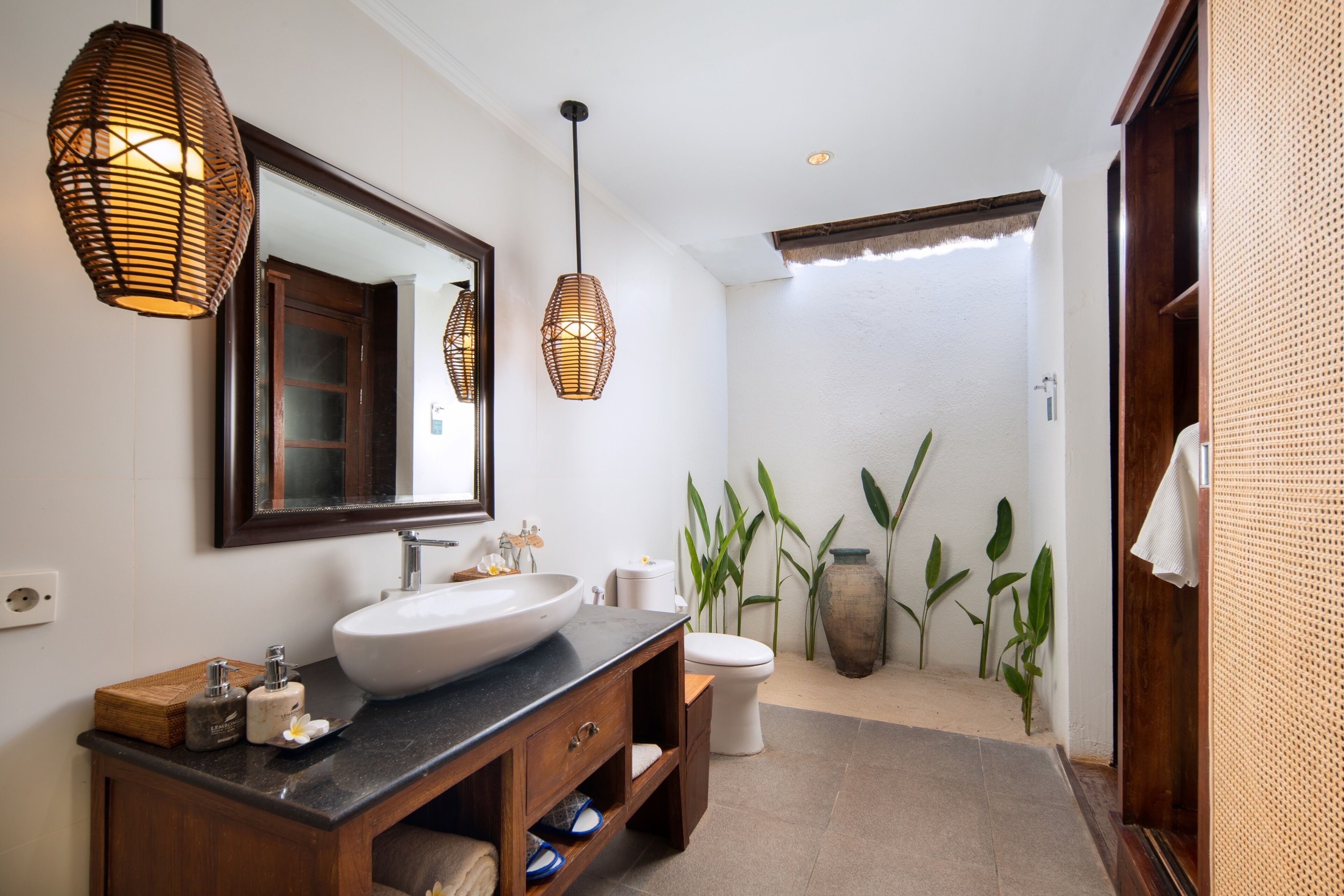 A modern bathroom with a large sink, wooden vanity, and two hanging wicker light fixtures.
