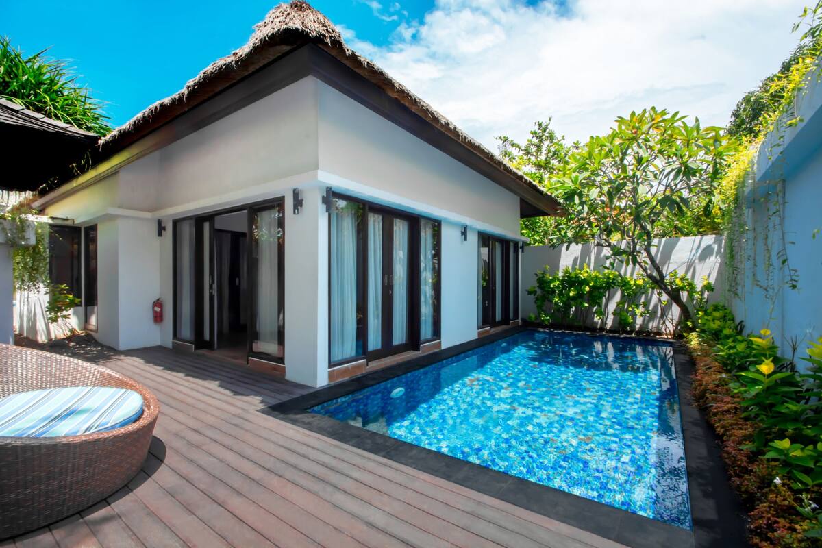 Une maison moderne dotée d’une piscine, de grandes fenêtres et d’un toit de chaume.