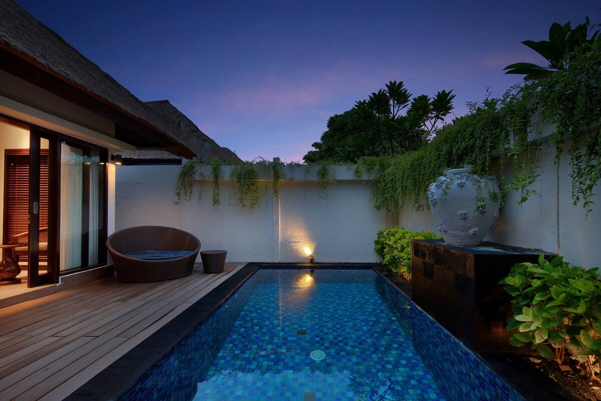 Une piscine avec une terrasse en bois, une chaise en osier et une plante en pot.