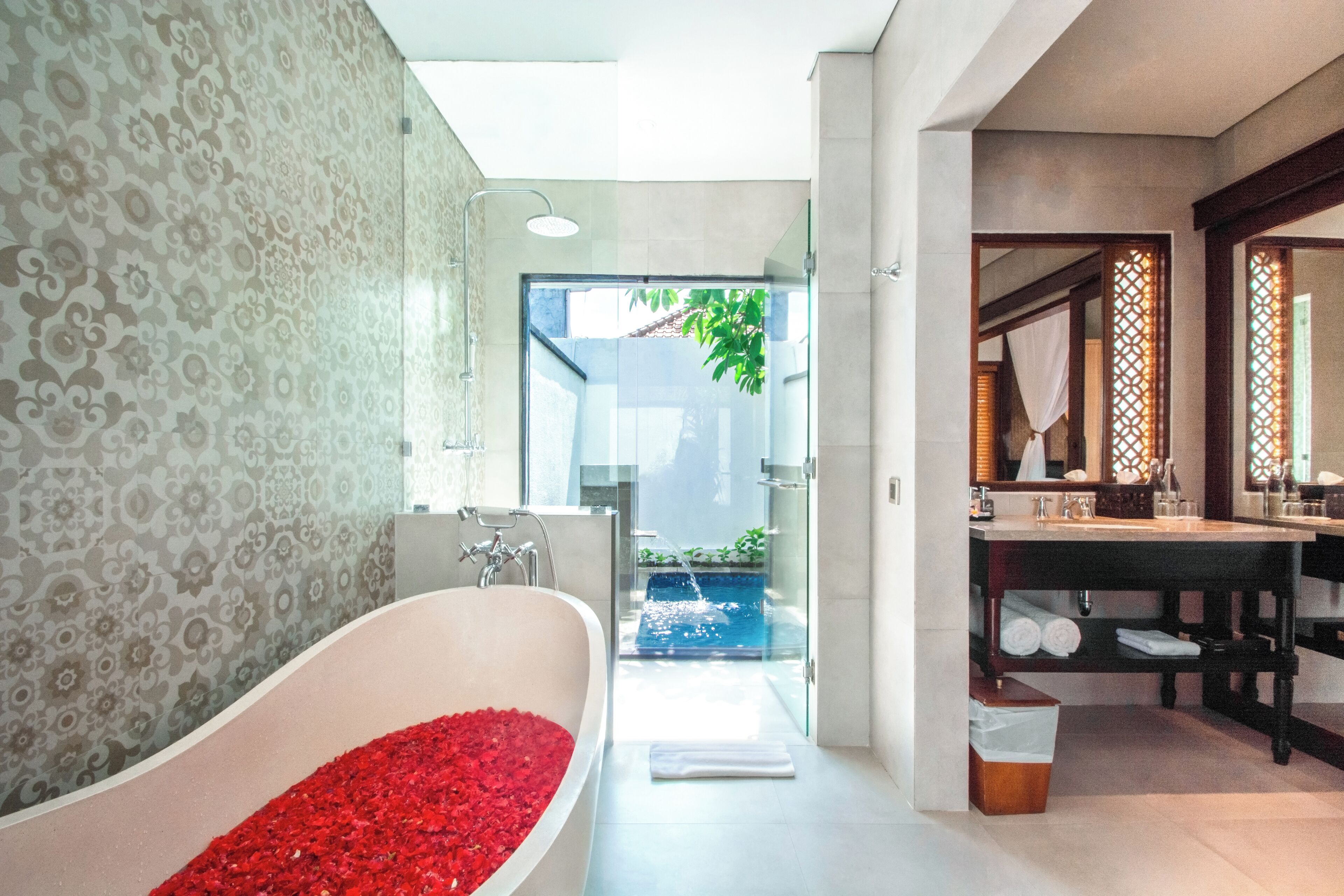 Une salle de bain moderne avec une baignoire sur pieds remplie de pétales de rose, une douche à parois de verre et un meuble-lavabo avec un miroir.