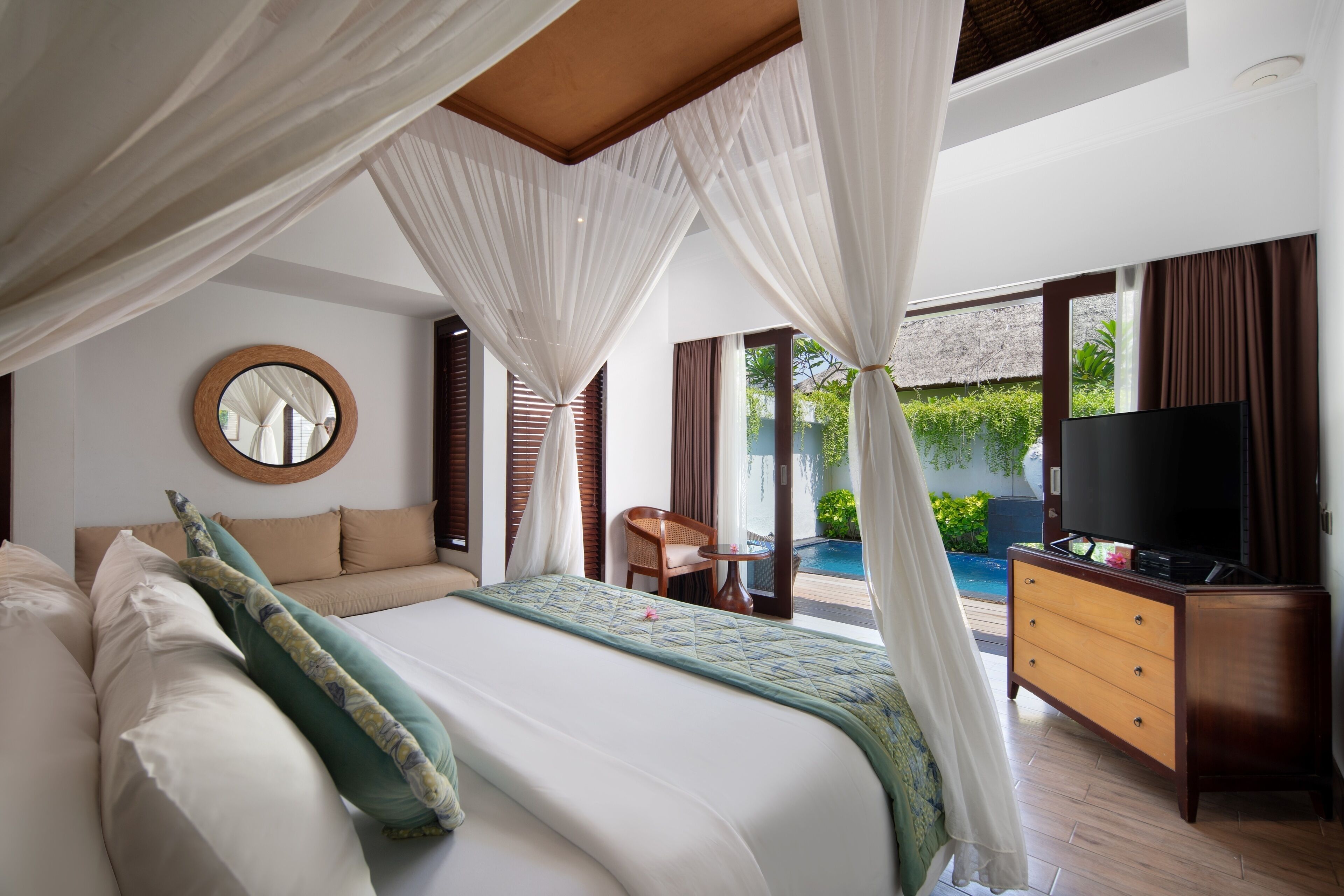 Un dormitorio con una cama grande, televisión, cómoda de madera y vista a una piscina.