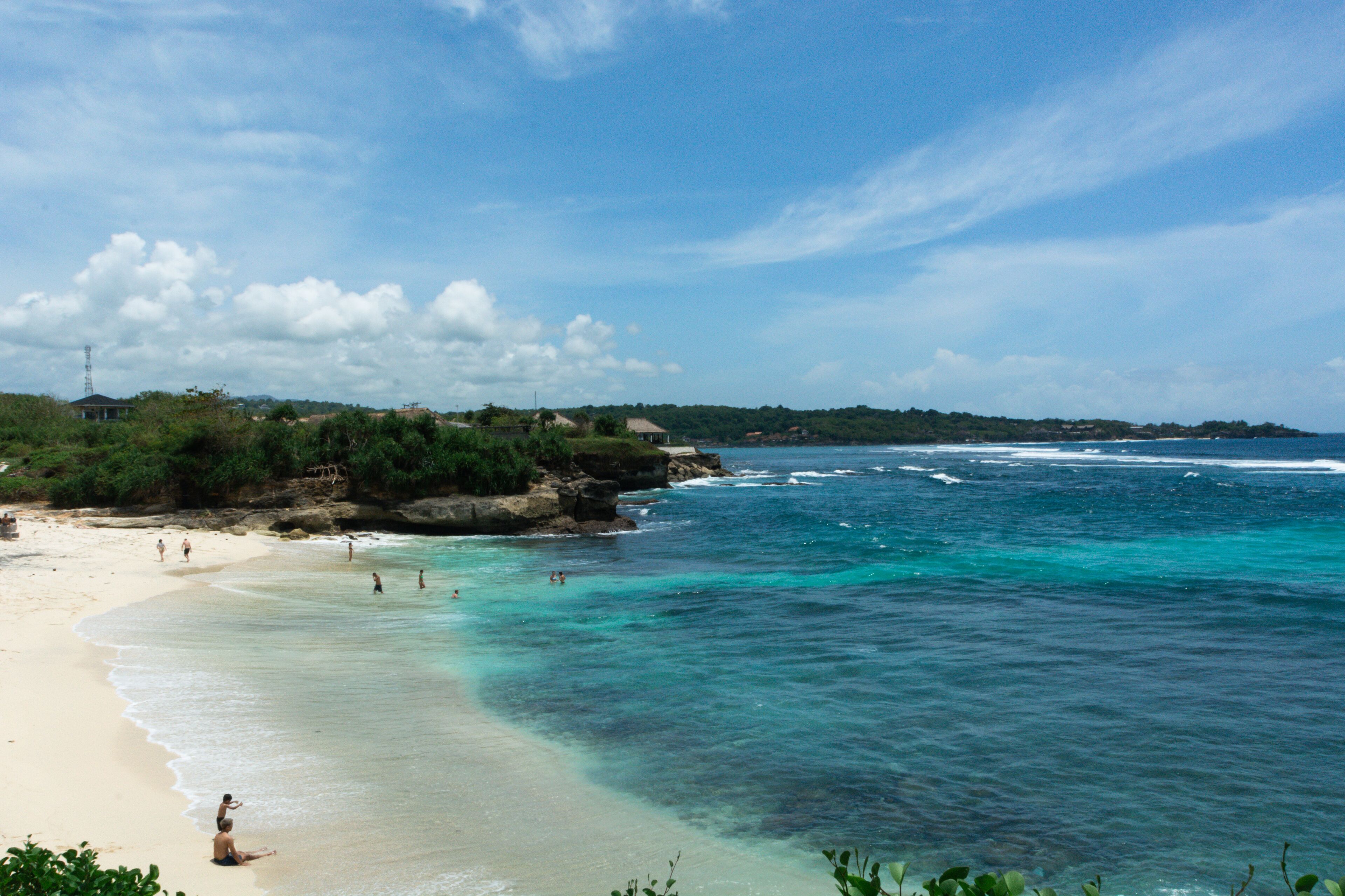 A beach with clear turquoise waters, sandy shore, and greenery in the background.