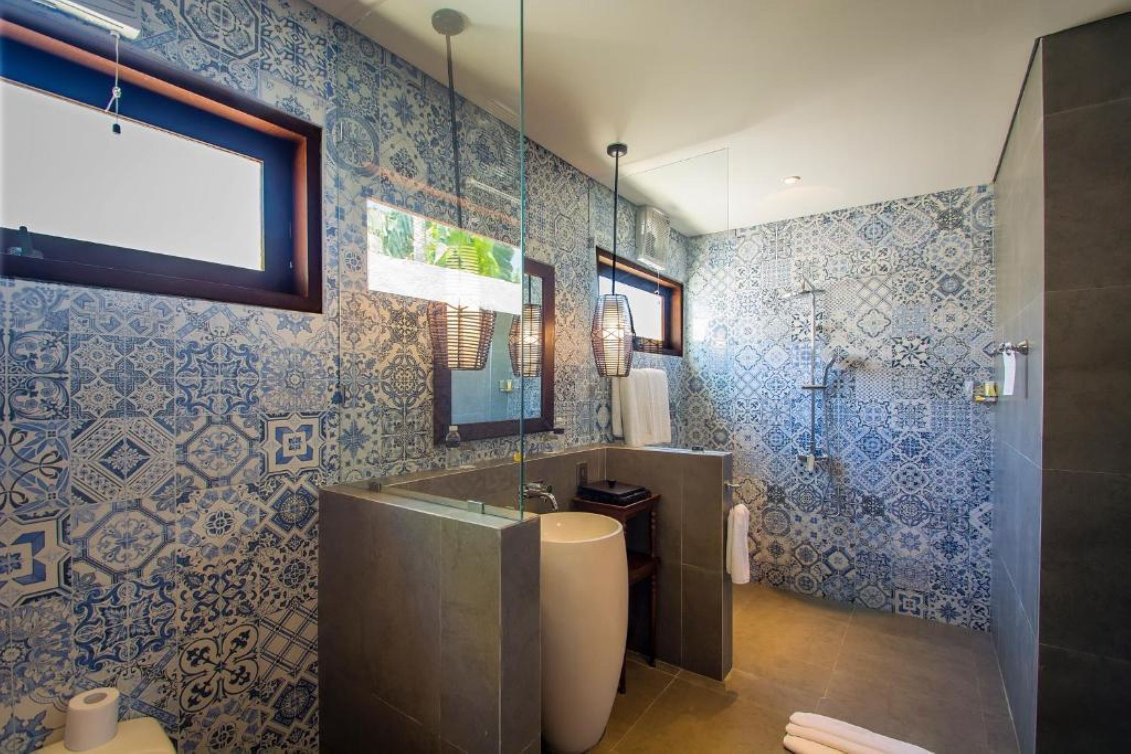 Un baño con azulejos de diseño azulado, un lavamanos amplio, un espejo y una zona de ducha.