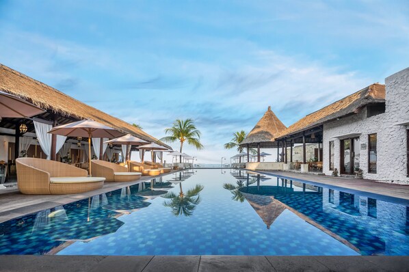 Relax by the serene pool surrounded by palm trees and lounge areas with cushioned seating.