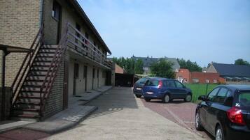 A building with a brick facade, a staircase, and a parking area with cars.