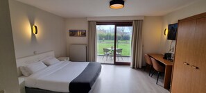Habitación de hotel con cama, escritorio, silla, televisor y vista al exterior.
