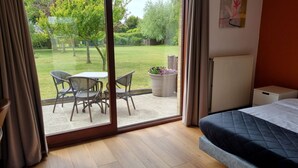 Un dormitorio con cama, ventana con cortinas, vistas a un jardín y una mesa con sillas.