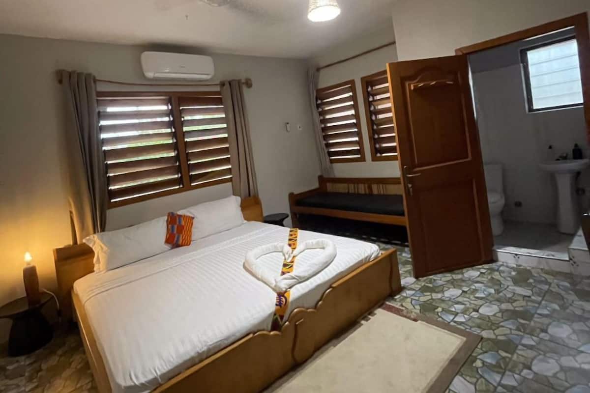 A bedroom with a bed, a bedside table, a nightstand, a ceiling fan, and a bathroom visible through an open door.