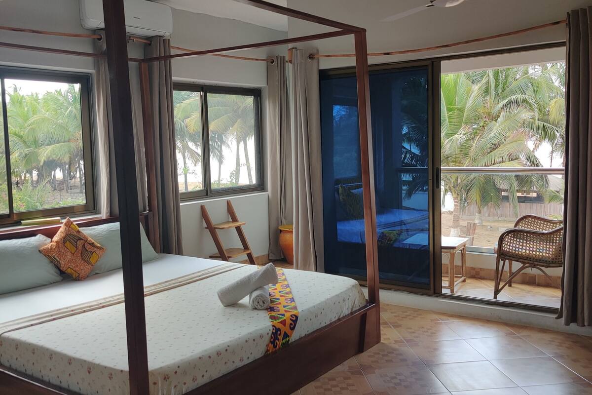 A four-poster bed with a view of palm trees through the window.