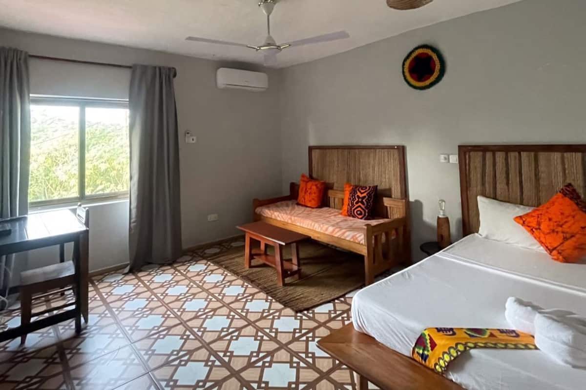 A hotel room with a bed, a desk, a chair, a ceiling fan, and a window with curtains.