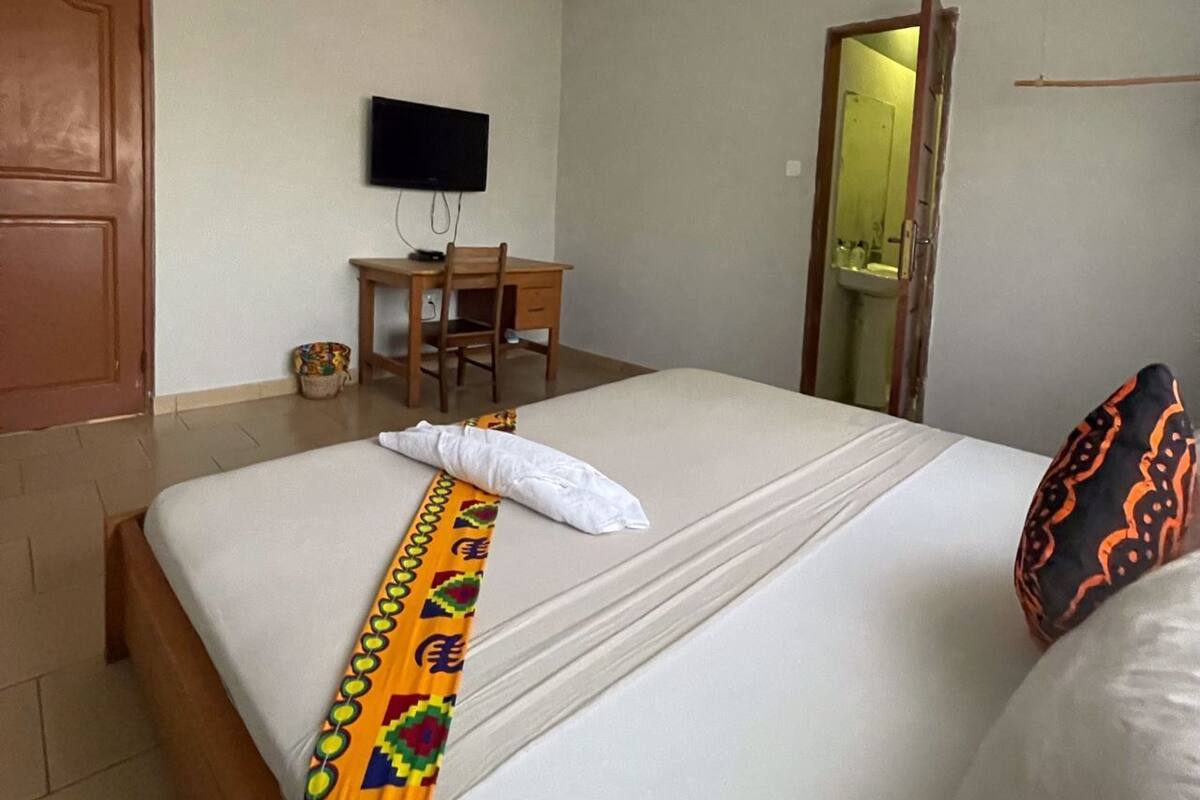 A hotel room with a bed, a desk, a television, and a bathroom visible through an open door.