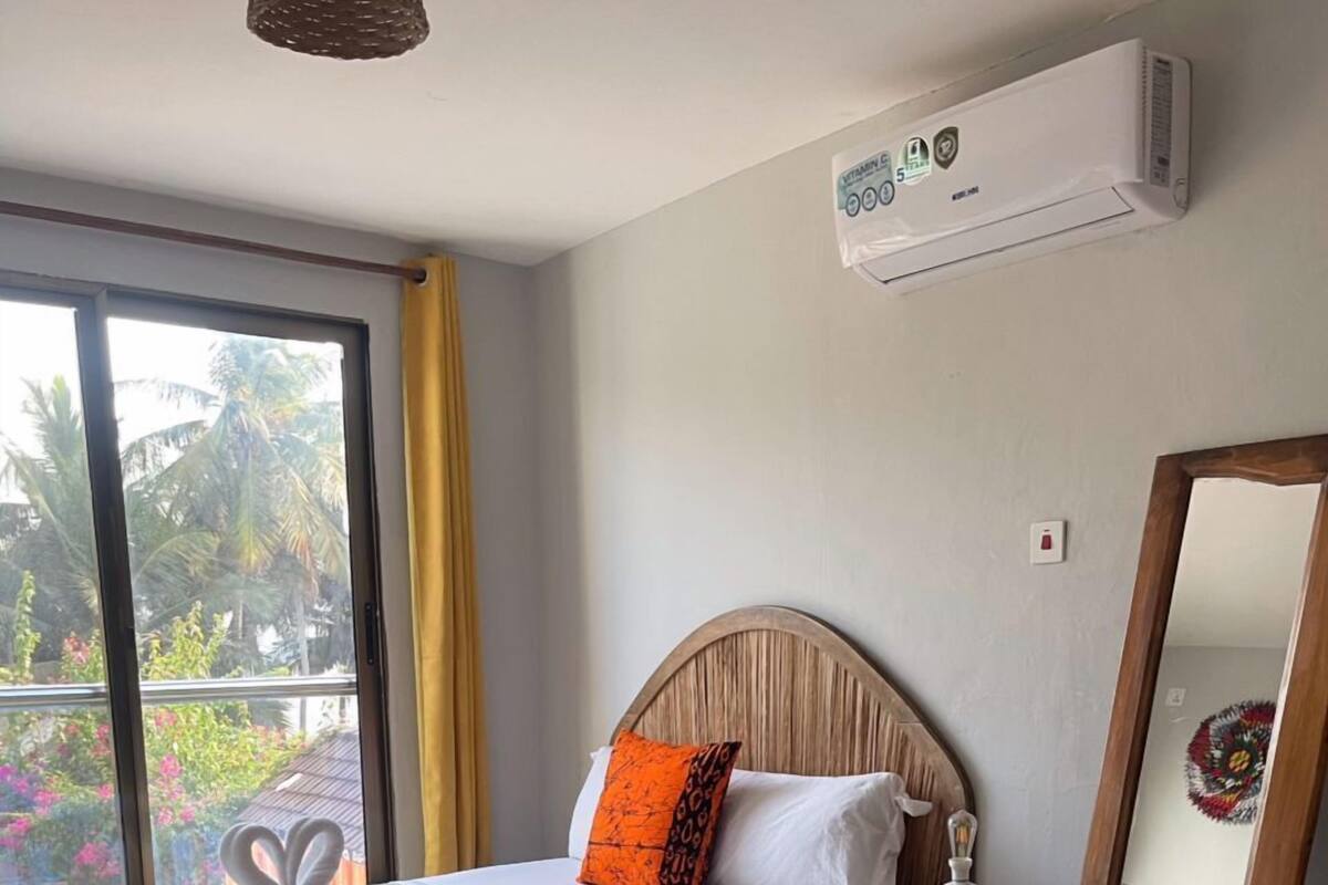 A hotel room with a bed, a round mirror, a small table, and an air conditioning unit on the wall.