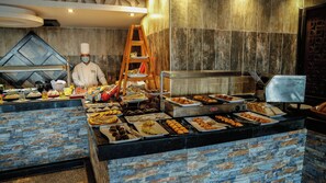 Zona de bufé con diversas opciones de comida y un chef preparando alimentos.