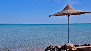 A clear blue sea with a rocky shore and a thatched umbrella structure. - Magic Beach Resort (Hurghada)