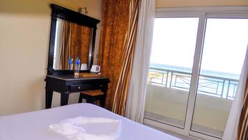 Habitación de hotel con cama, escritorio con espejo, cafetera y vista al mar desde el balcón.