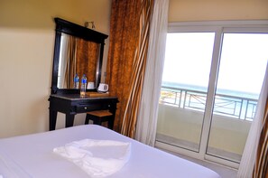 A hotel room with a bed, a desk with a mirror, a coffee maker, and a view of the sea through a balcony door. - Magic Beach Resort (Hurghada)