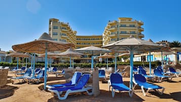 Resort à beira-mar com espreguiçadeiras e guarda-sóis, piscina e um edifício de hotel ao fundo.
