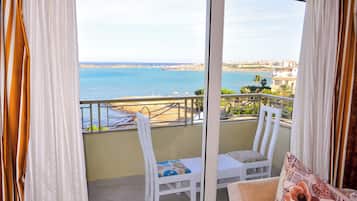 A balcony with a view of the sea and a bridge, white chairs, and a cushion.
