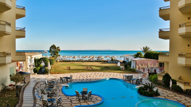 A pool area with lounge chairs and umbrellas, a view of the beach, and a clear sky. - Magic Beach Resort (Hurghada)