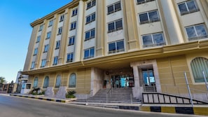 Een hotel met meerdere verdiepingen, een opvallende ingang en een trap die naar de ingang leidt, onder een heldere hemel.