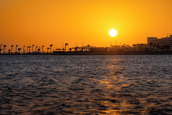 A sunset over a body of water with a pier and buildings in the background. - Magic Beach Resort (Hurghada)