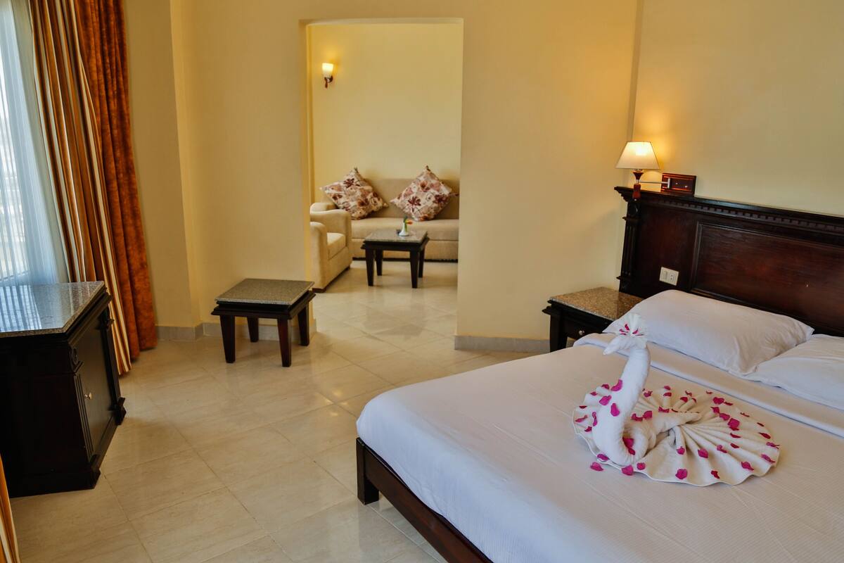 A hotel room with a bed, a nightstand, a bedside table, a chair, and a sofa.