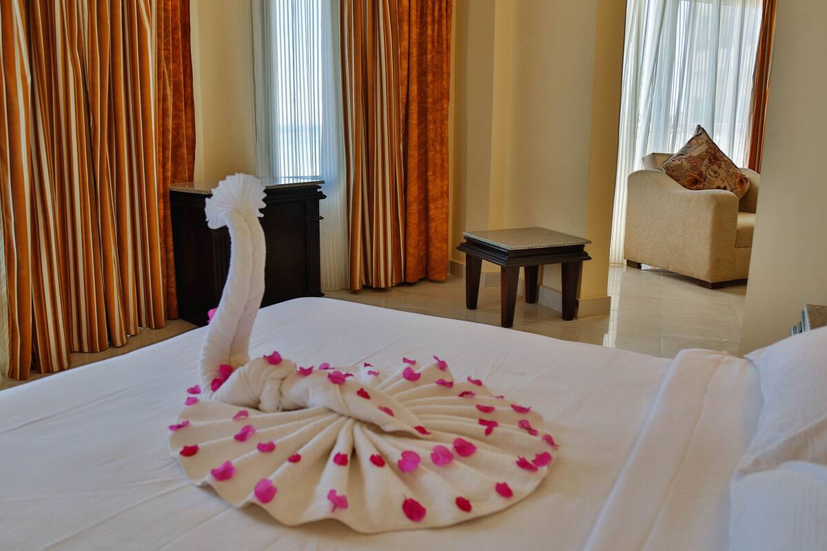 A hotel room with a neatly made bed, a small table, a chair, and curtains.