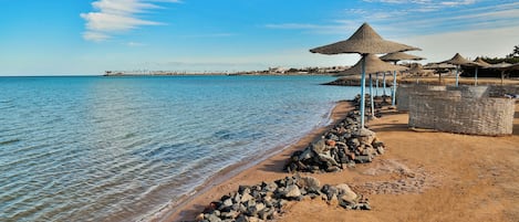A beach with clear blue water, a rocky shoreline, and thatched umbrellas.