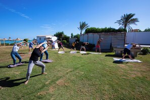 Um grupo de pessoas praticando yoga ao ar livre em um campo gramado sob um céu claro.