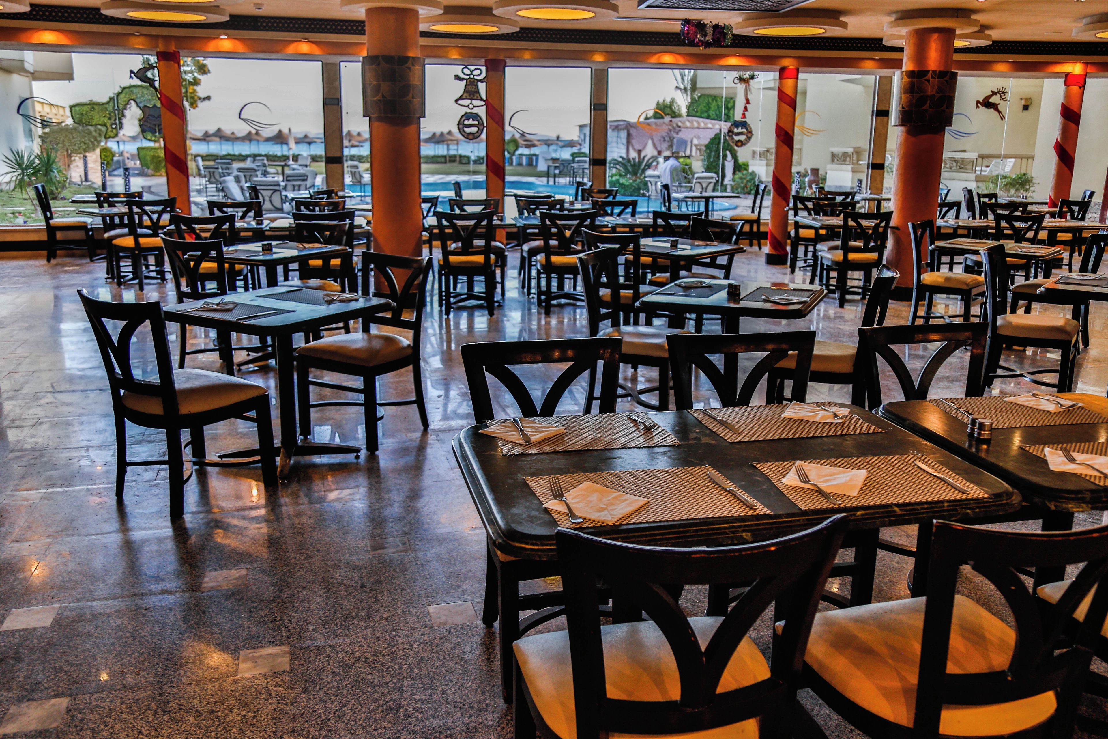 A restaurant with multiple tables and chairs, large windows, and a view of the outdoors.