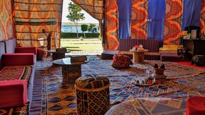 Ein Zimmer mit gemusterten Teppichen, roten Kissen, einem kleinen Tisch und Blick auf einen Strand.