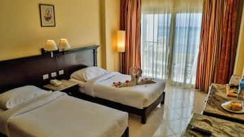 Quarto de hotel com duas camas, telefone ao lado da cama, luminária e vista para o exterior através de cortinas.