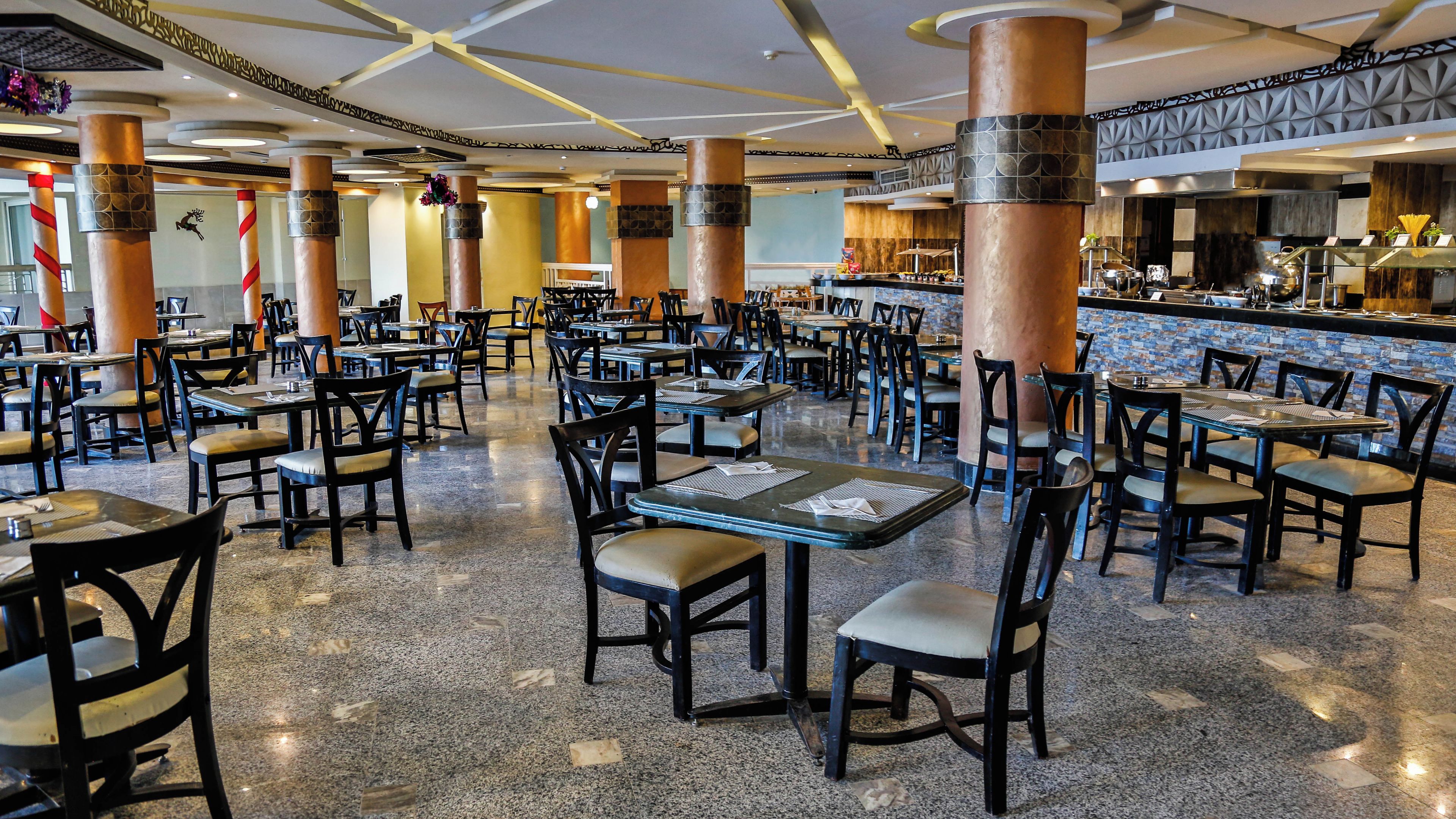 A spacious restaurant with multiple tables and chairs, high ceilings, and decorative columns.