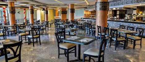 A spacious restaurant with multiple tables and chairs, high ceilings, and decorative columns.