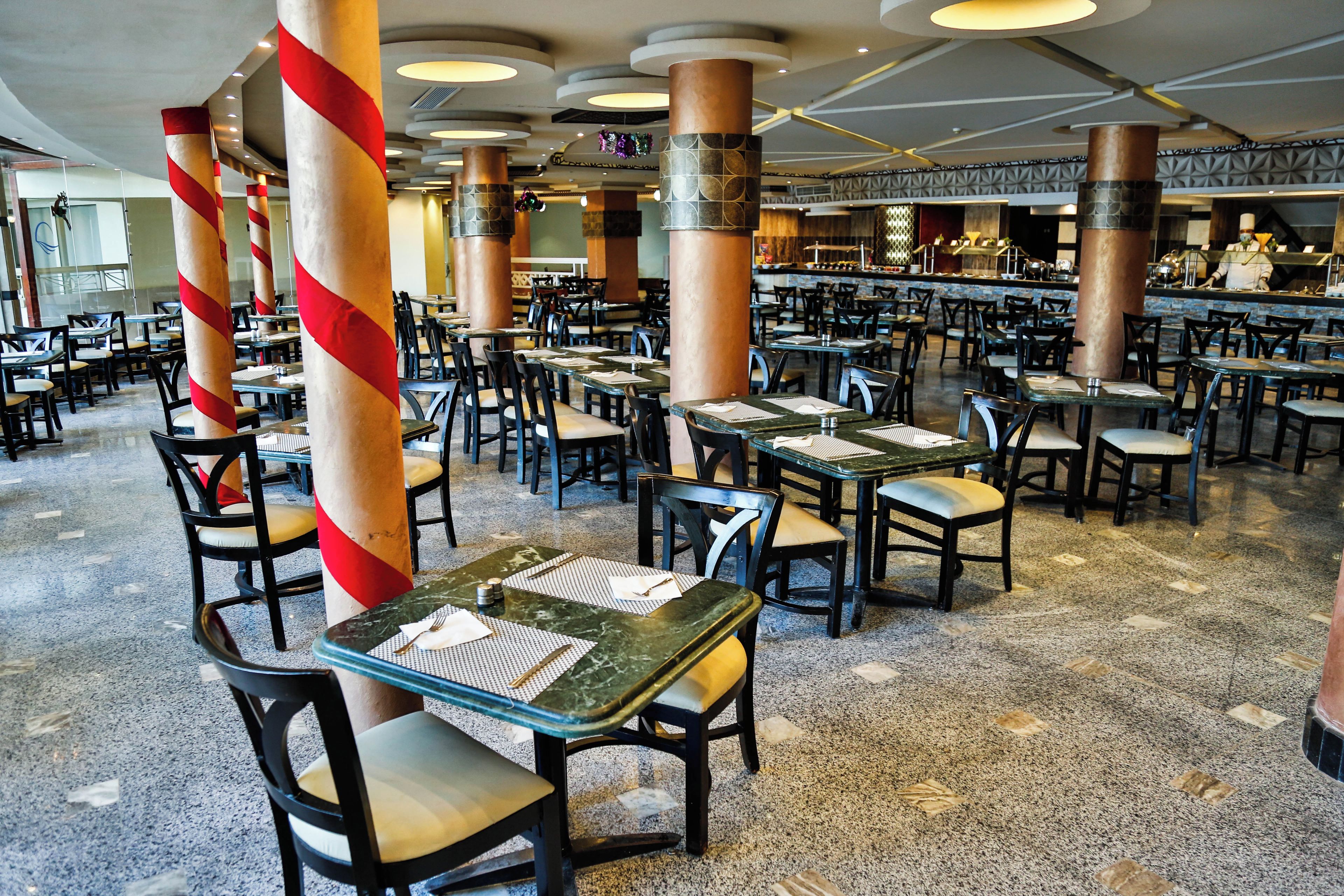 Un ristorante spazioso con diversi tavoli e sedie, caratterizzato da un design moderno con ampie colonne e pavimento lucido.
